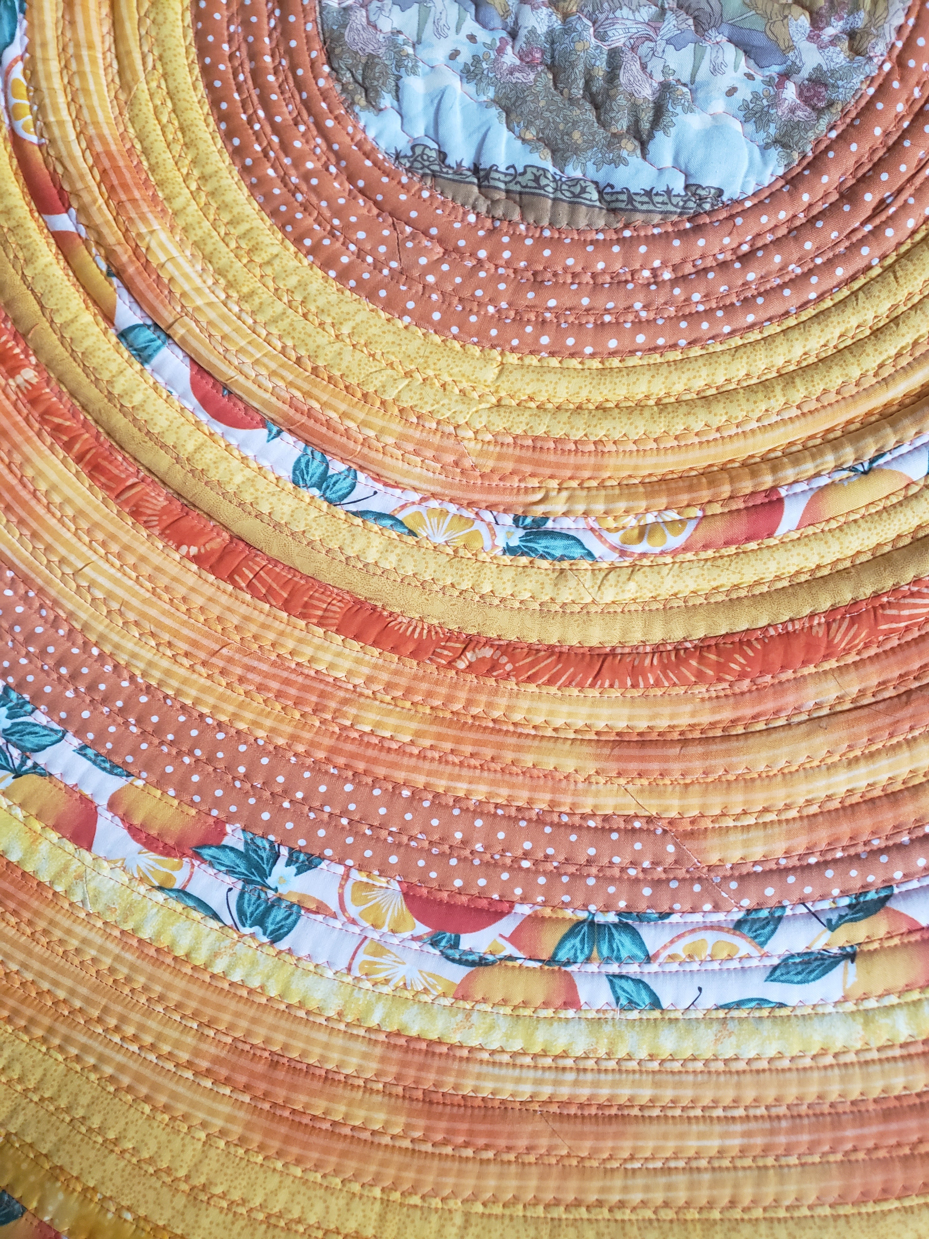 Detail of orange, yellow, and citrus print fabric coils on handmade rug